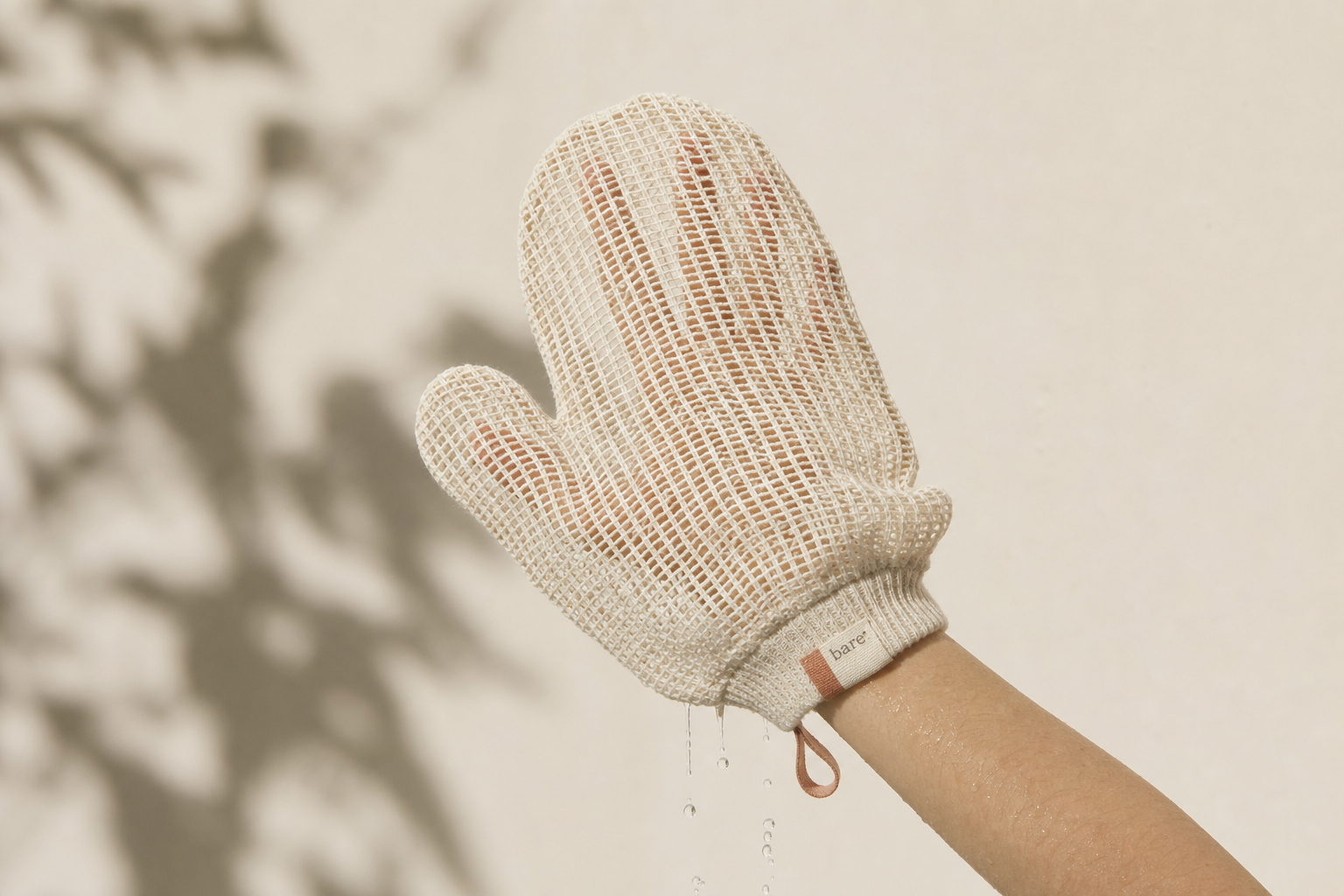 the mitt — open-weave plant-fiber scrub mitt worn on a hand under running water, with a clay bare. tab and hang loop